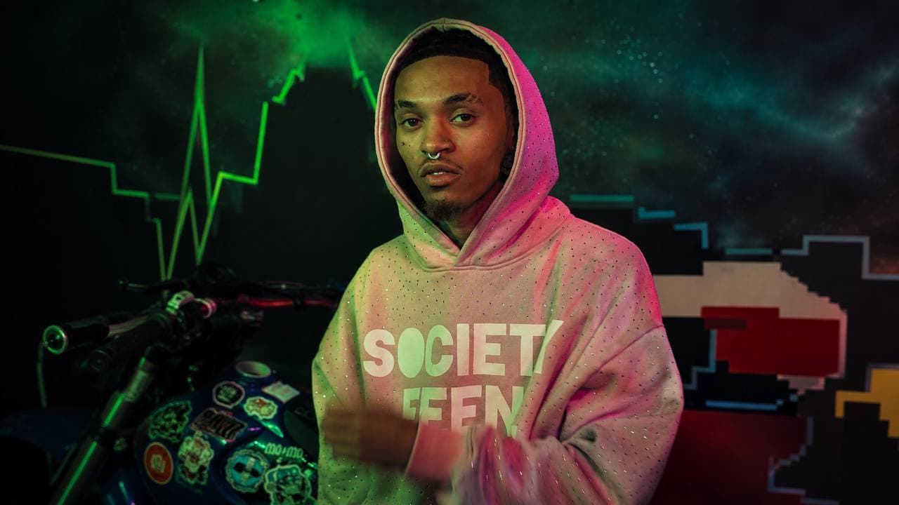 Lanrete Alone in a pink Society Feen hoodie against a dark, colorful studio backdrop.